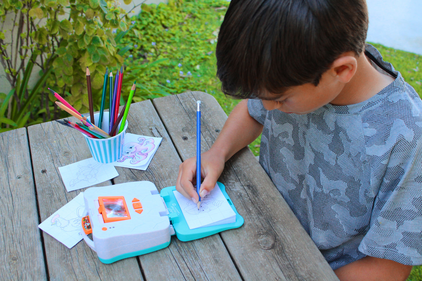 ילד מצייר באמצעות מקרן חכם לדרך !smART Sketcher® GO תוך כדי ישיבה על שולחן פיקניק בחוץ
